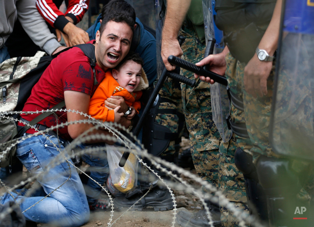 FOR USE AS DESIRED, YEAR END PHOTOS - FILE - A migrant man and a boy react as they are stuck between Macedonian riot police officers and migrants during a clash near the border train station of Idomeni, northern Greece, as they wait to be allowed by the Macedonian police to cross the border from Greece to Macedonia, Friday, Aug. 21, 2015. Macedonian special police forces fired stun grenades to disperse thousands of migrants stuck on a no-man's land with Greece, a day after Macedonia declared a state of emergency on its borders to deal with a massive influx of migrants heading north to Europe. (AP Photo/Darko Vojinovic, File)